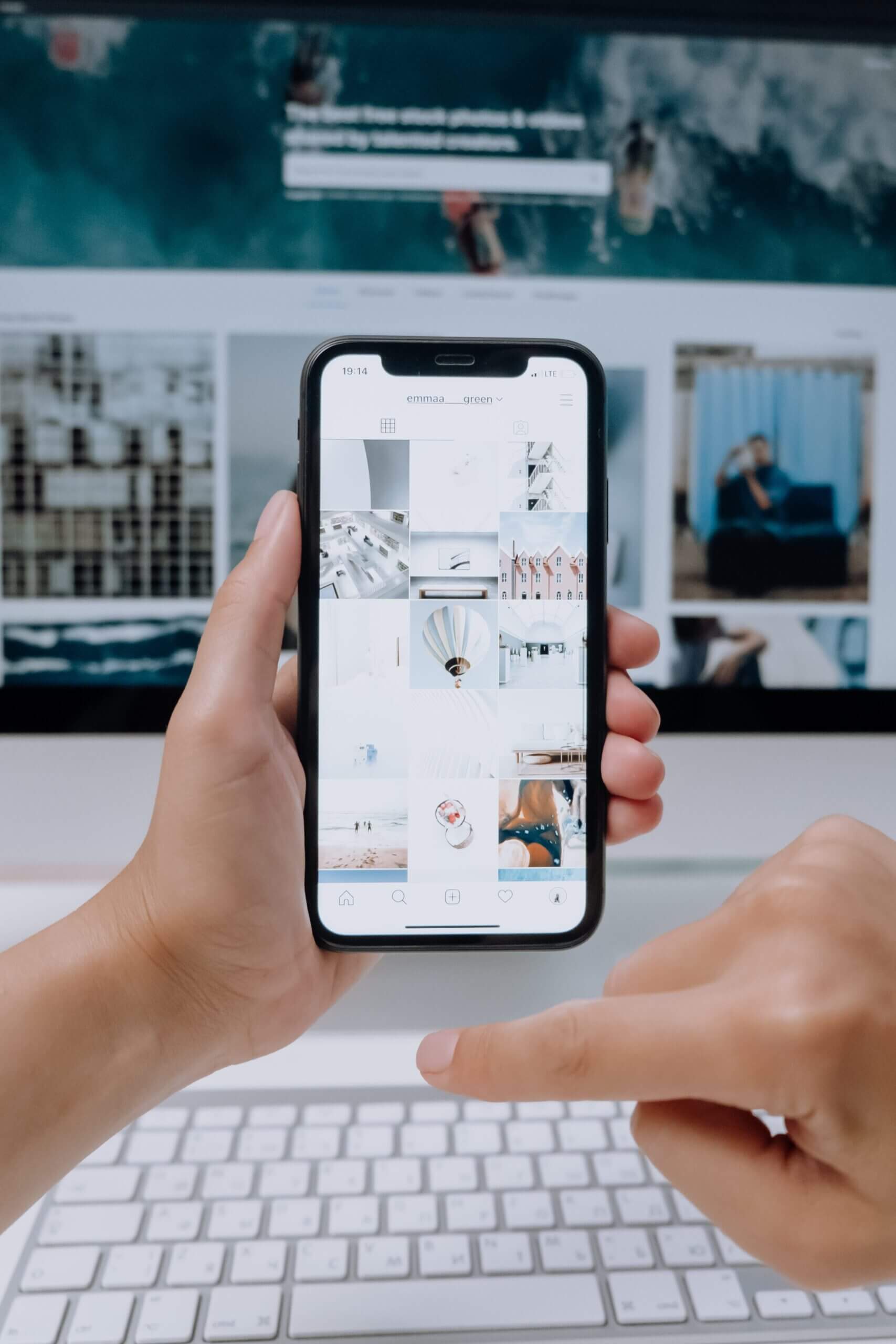 Un personne tient un smartphone devant un ordinateur